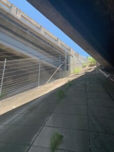An electric chain link fence surrounds a sidewalk under a bridge