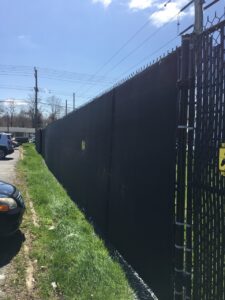 A black chain link fence with a yellow warning sign on it
