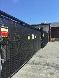 A black chain link fence with a yellow warning sign on it