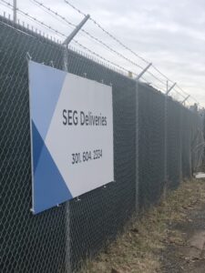 A Sign on a Chain Link Fence says "SEG Deliveries"