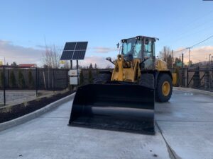 A bulldozer is parked on a concrete surface next to a solar panel