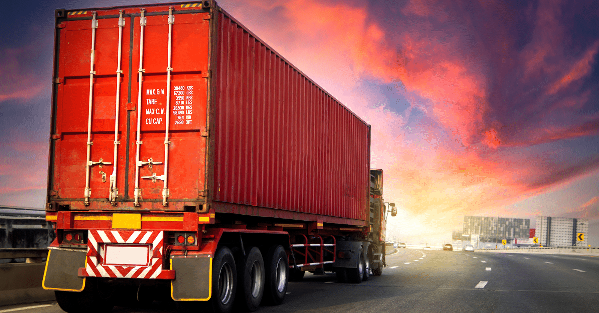 a red semi truck is driving down a highway at sunset