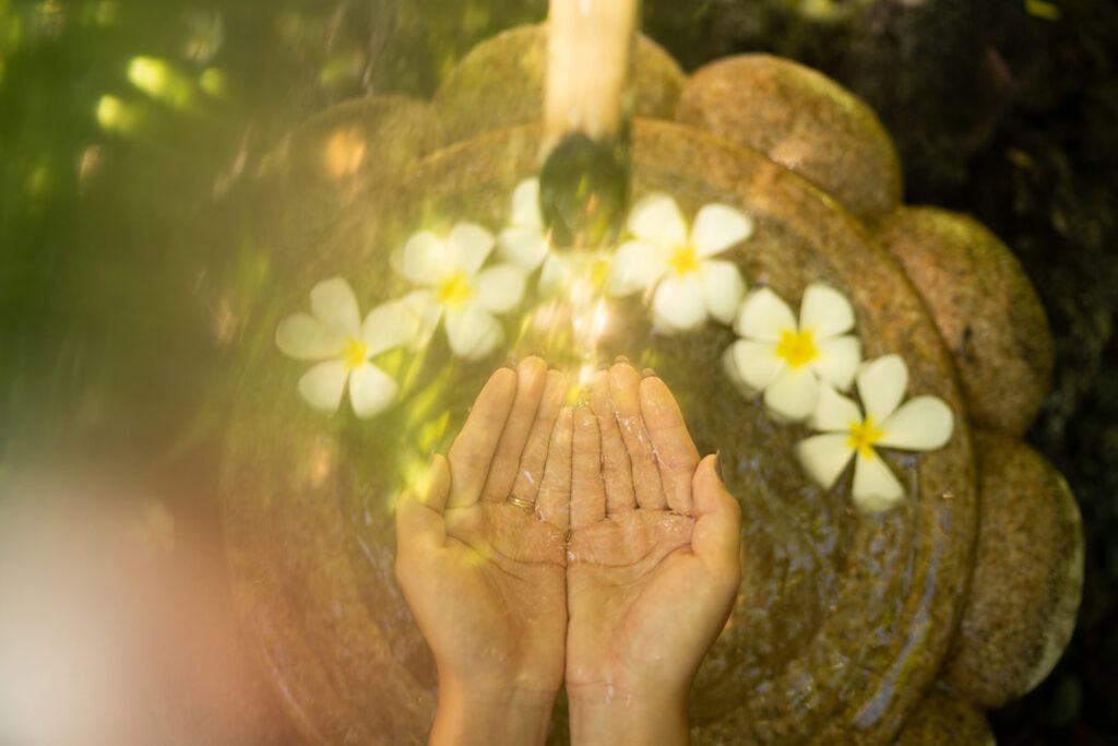 A Woman is Holding Water in Her Hands in Front of Flowers